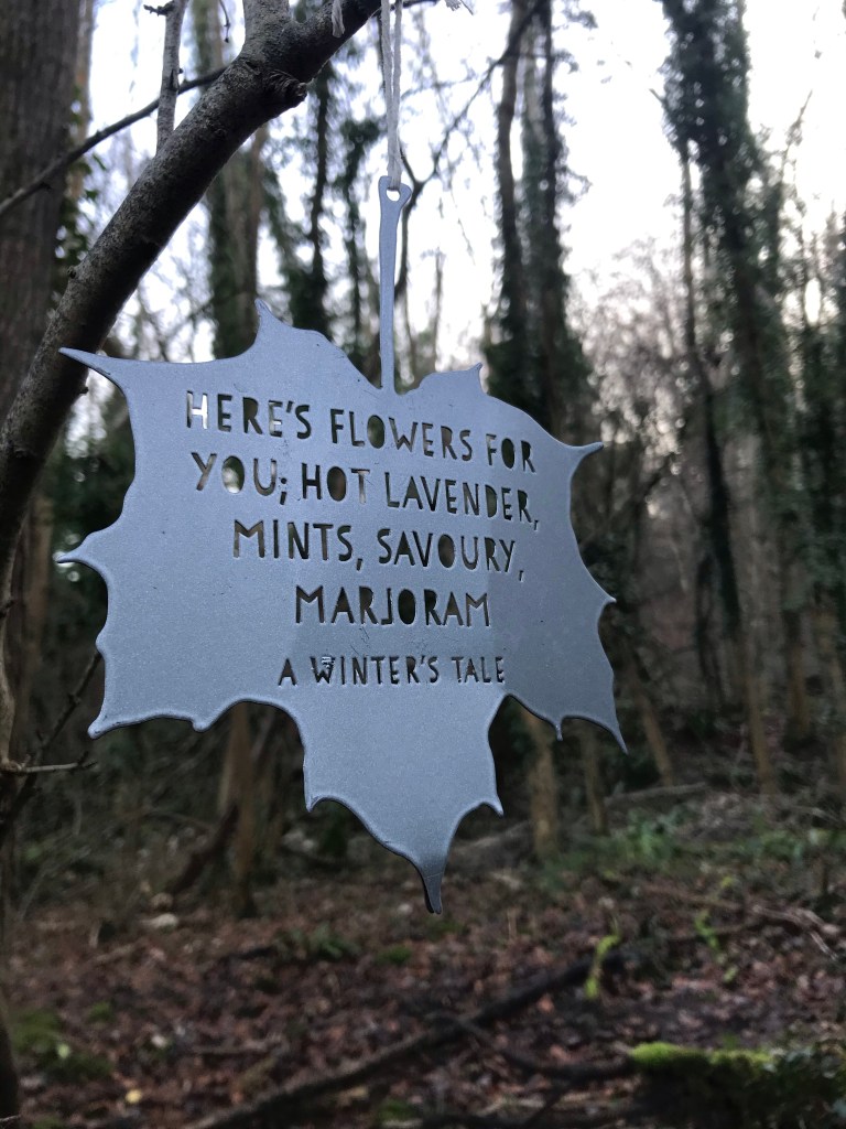 a metallic leaf hanging from a tree with words from The Tempest engraved on it