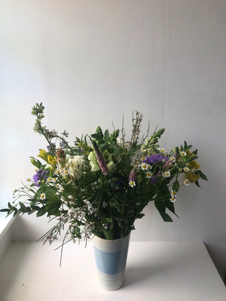 The image is of various different types of flowers in a small blue and white vase