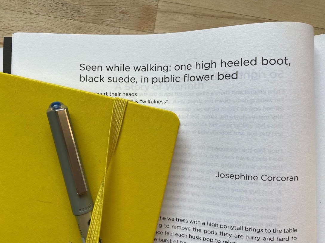 The image shows a published poem by Josephine Corcoran hidden behind a yellow notebook and a pen