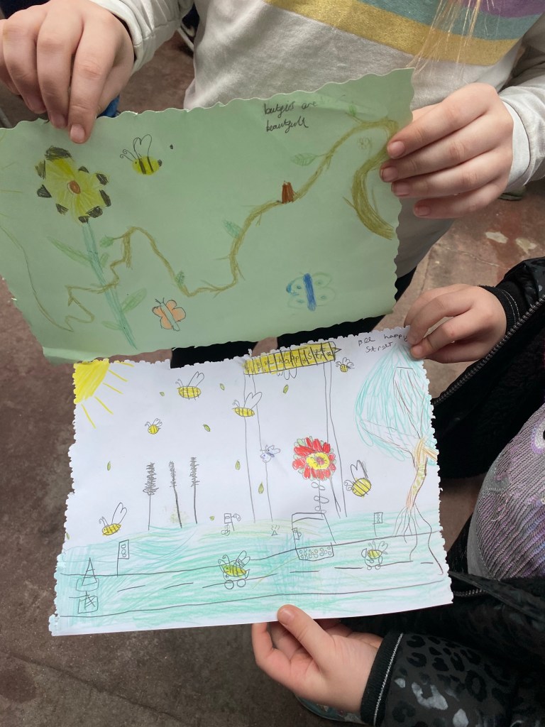 child's hands holding up their pictures of flowers and insects